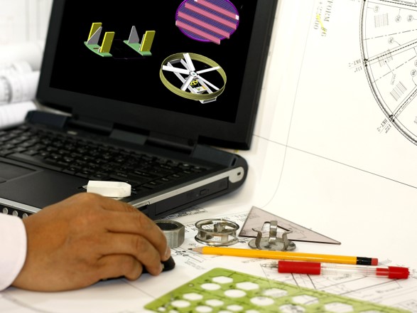 Photo of technical drawing materials and a CAD model on a laptop