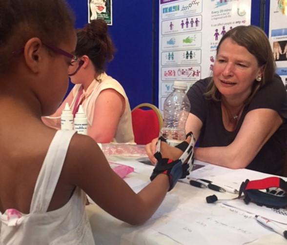Photo of a child holding a water bottle while wearing a simulation glove, at a stand at the science festival