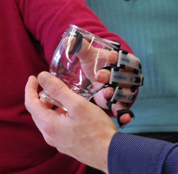 an older person holding a glass while wearing simulation gloves