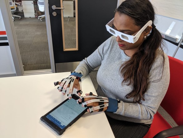 A woman wearing simulation gloves and glasses and trying to use a tablet computing device