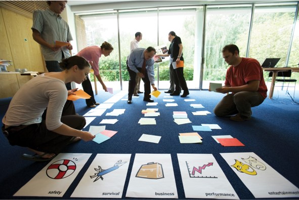 photograph showing a group of people laying out various cards on the floor, within a grid-like structure